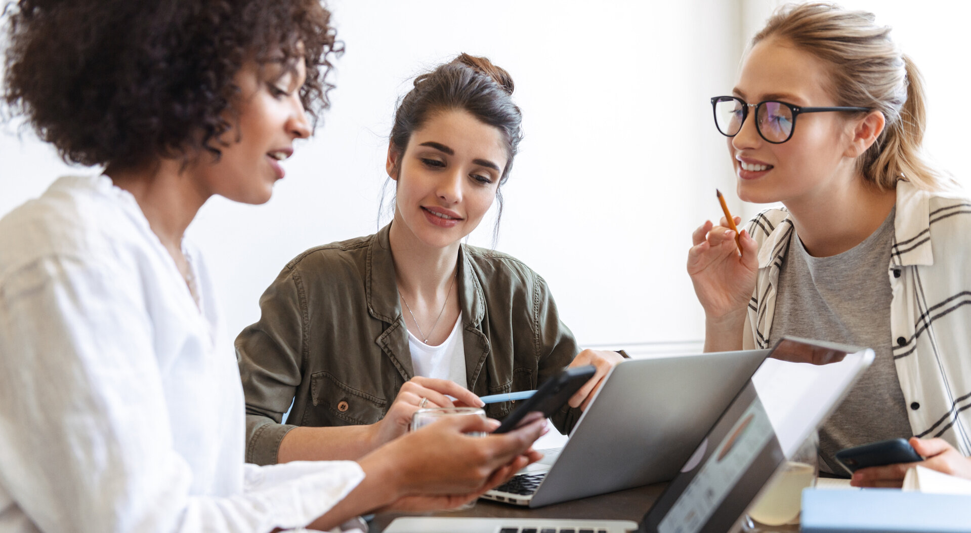 Drei Frauen arbeiten gemeinsam mit Laptop und Notizen an einem Tisch und tauschen sich aus