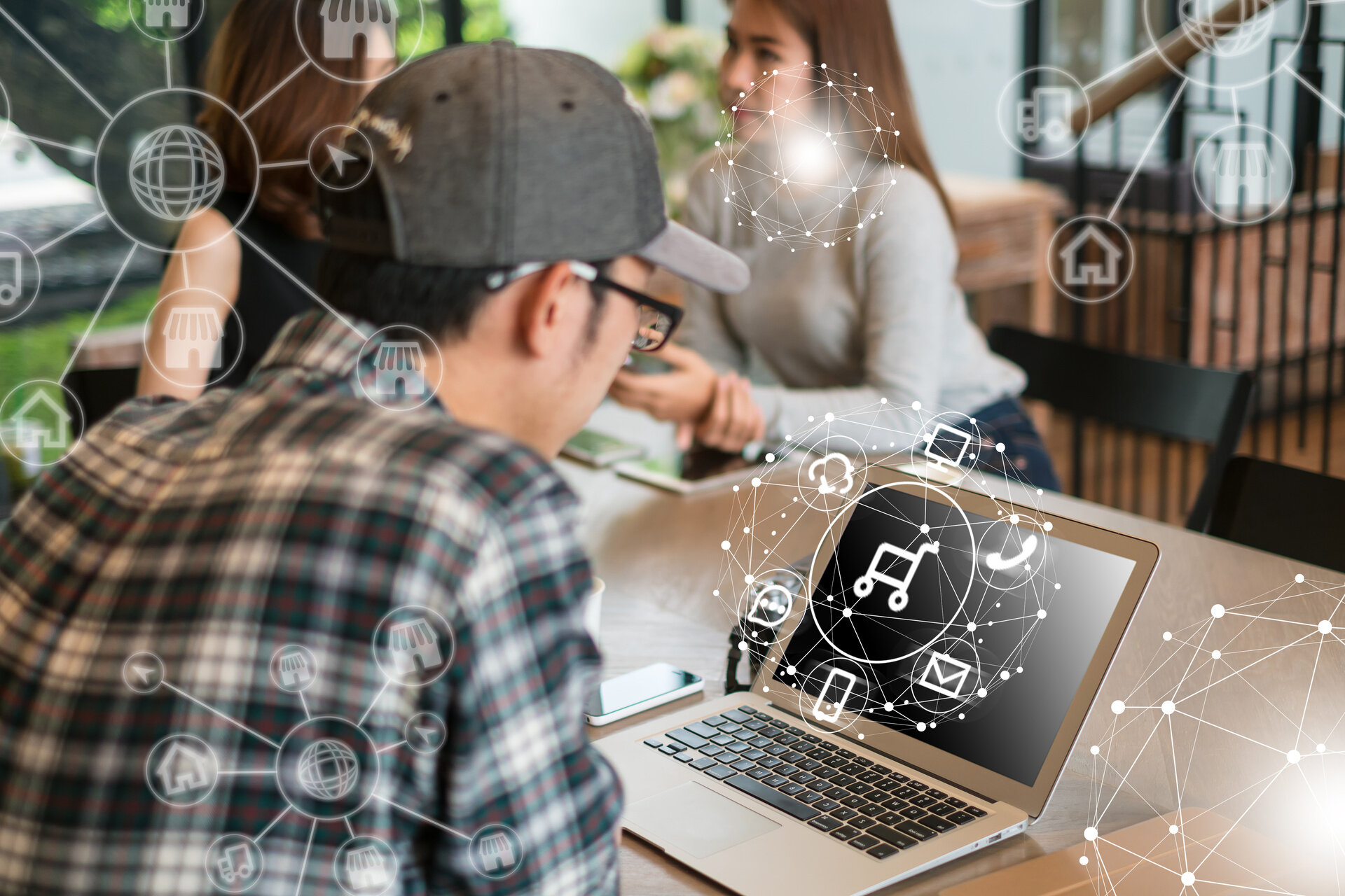 Person arbeitet am Laptop mit E-Commerce-Symbolen, während im Hintergrund digitale Vertriebs- und Handelsprozesse im Team besprochen werden
