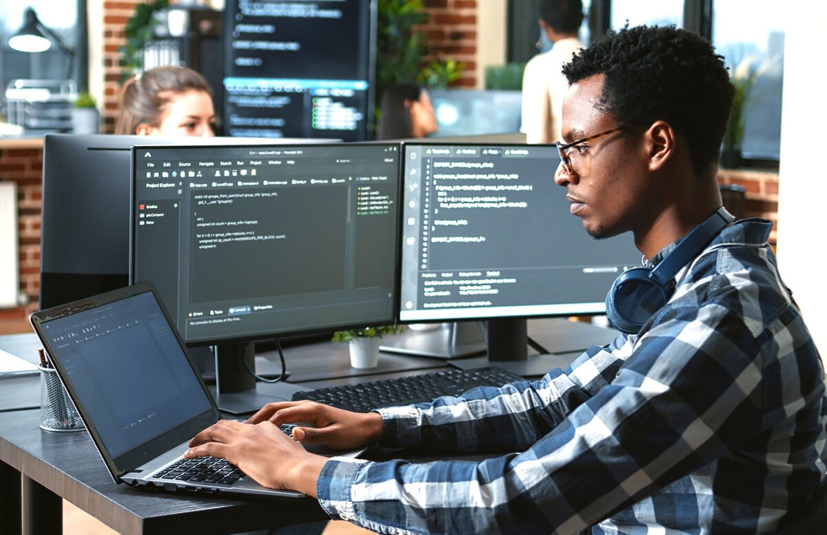 Fachinformatiker arbeitet an mehreren Bildschirmen und einem Laptop