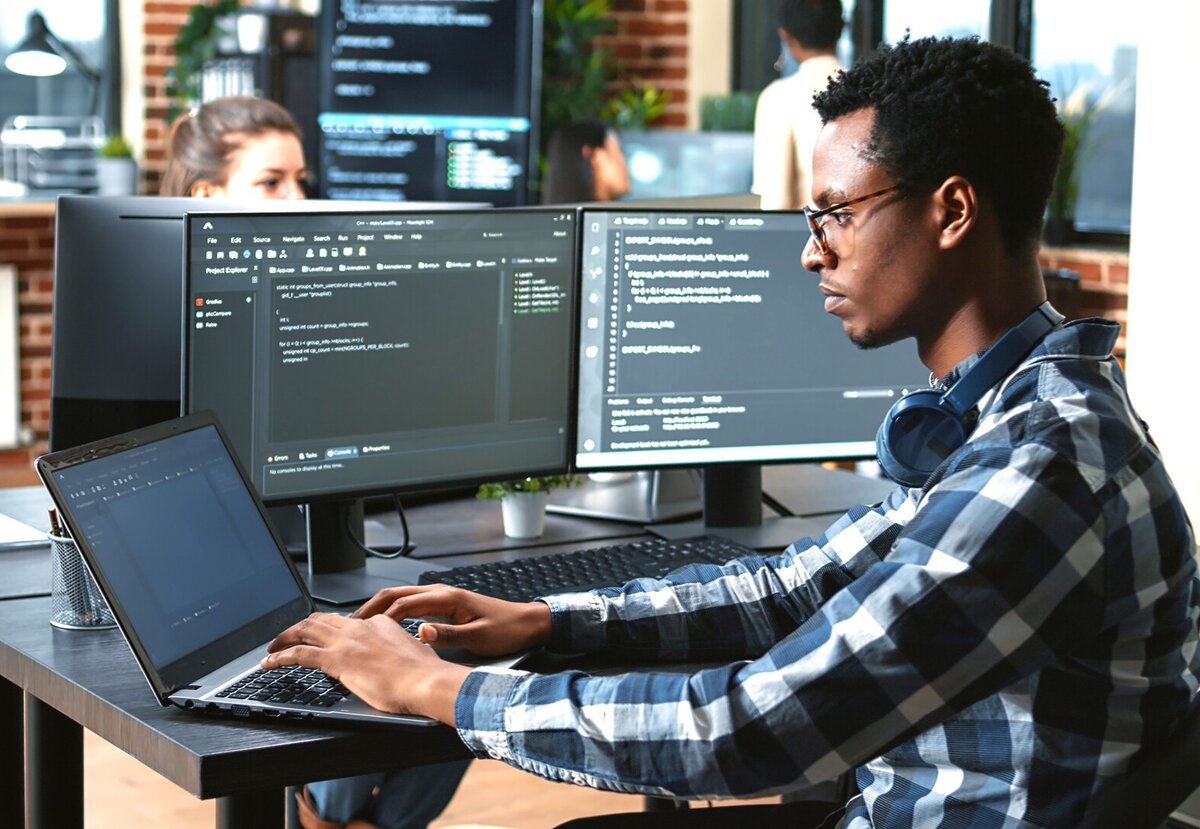 Fachinformatiker arbeitet an mehreren Bildschirmen und einem Laptop