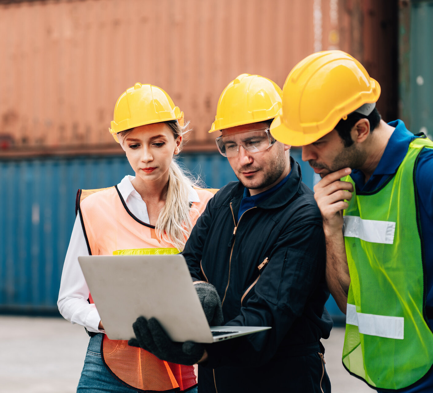 Team bespricht Arbeitsabläufe mit einem Laptop in einem Industrie- und Logistikumfeld
