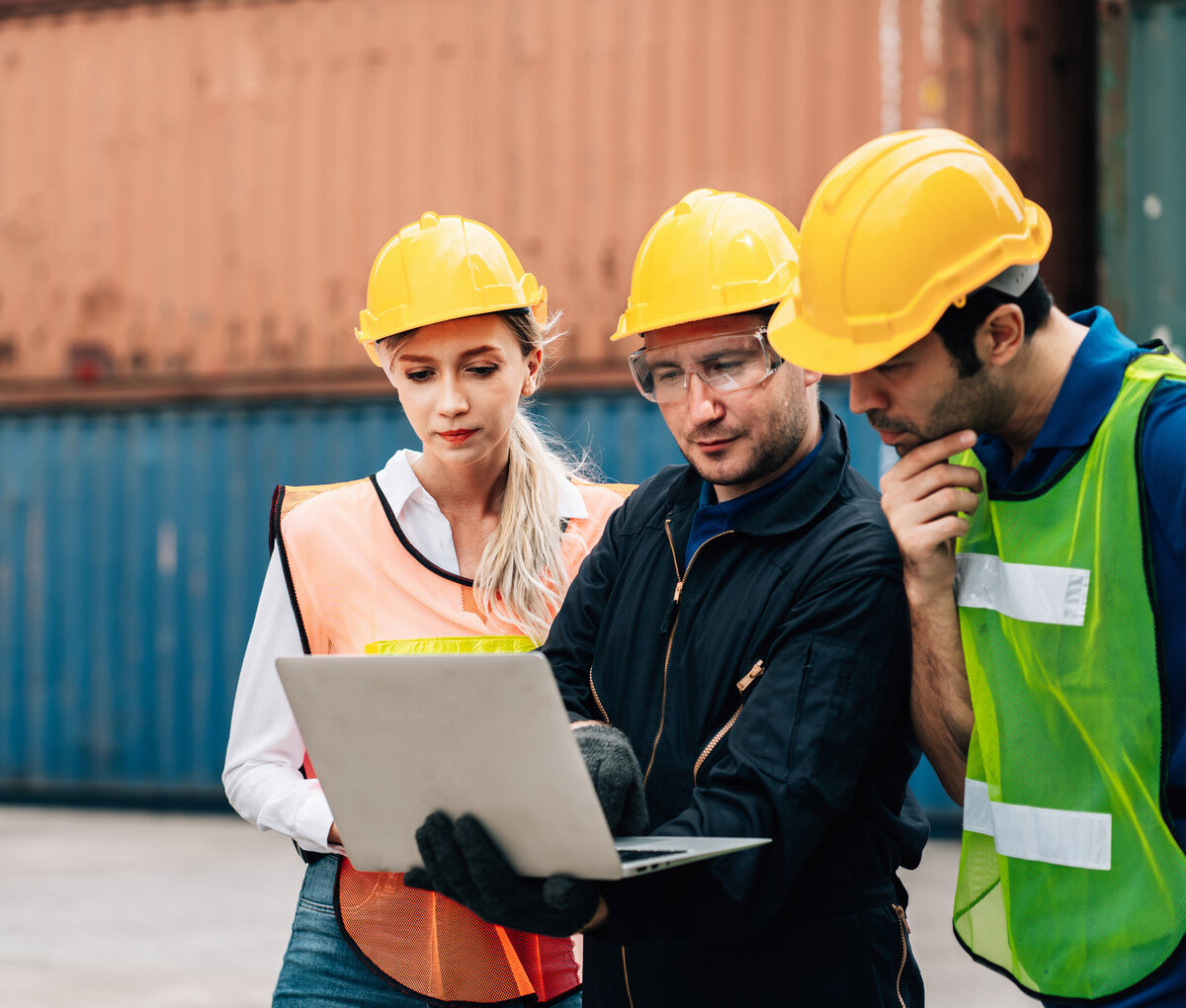 Team bespricht Arbeitsabläufe mit einem Laptop in einem Industrie- und Logistikumfeld