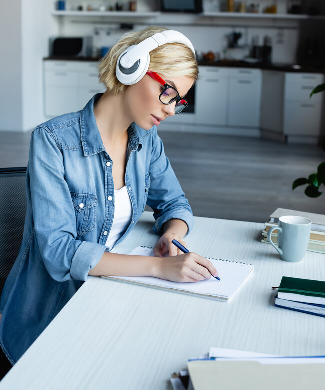 Frau mit Kopfhörern lernt online und macht Notizen für eine Weiterbildung 