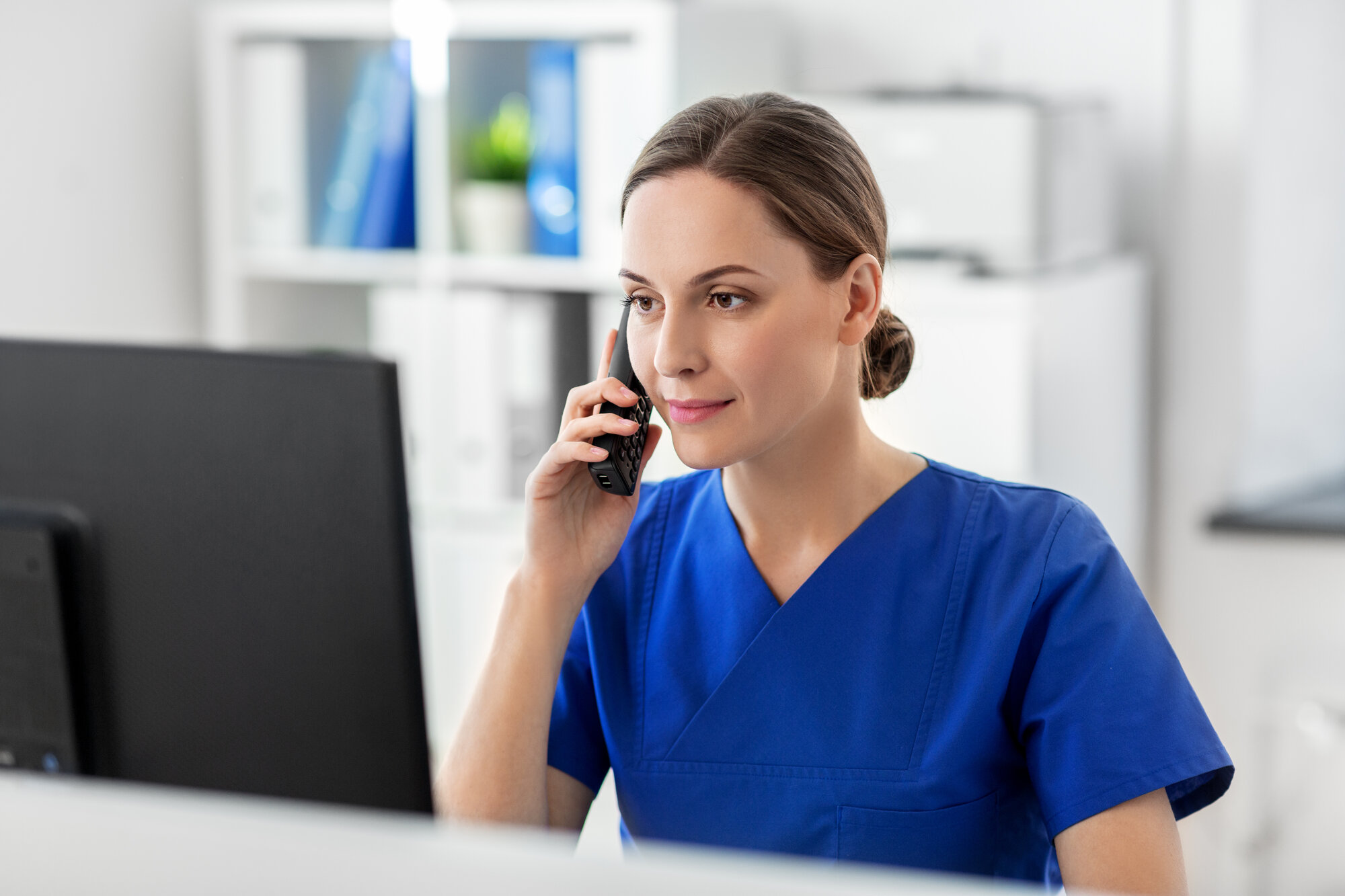 Umschulung Kaufmann/-frau im Gesundheitswesen (IHK) Mitarbeiterin im Gesundheitswesen telefoniert an einem Computerarbeitsplatz